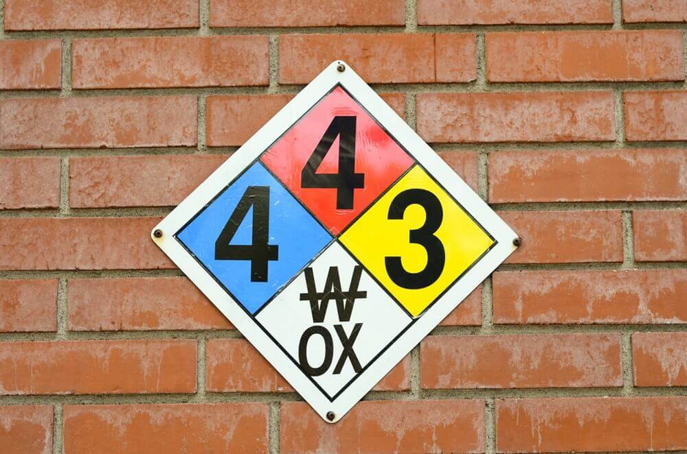 NFPA fire diamond posted on a brick wall. The fire diamond is a white diamond with four colored diamonds inside it all representing the hazards associated with various chemicals.